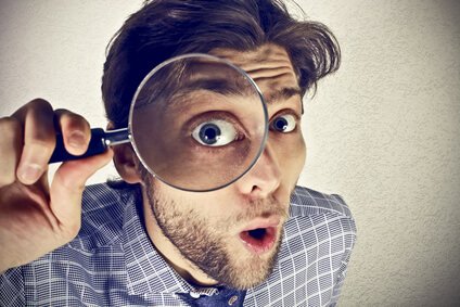 Mann hält eine Lupe vor sein Auge, das vergrößert erscheint. Symbolbild für Sehprobleme und Kurzsichtigkeit.